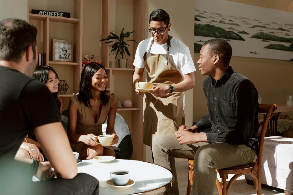 A group of friends enjoying coffee served by a waiter in a cozy café setting.