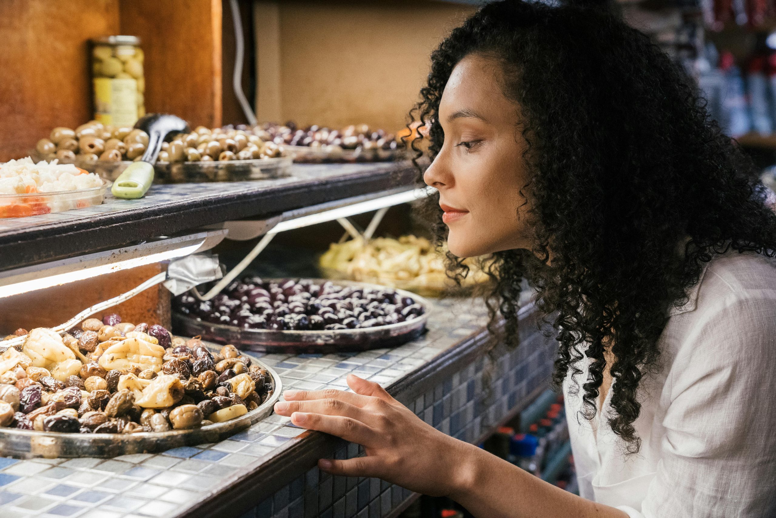 A woman observes a display filled with a variety of olives and other foods.